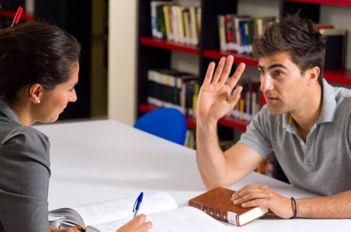 man-talking-to-woman-with-hand-up-near-shelf-of-books